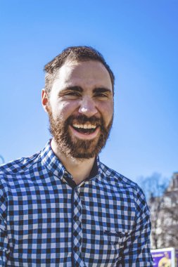 Portre genç adam parkta açık mavi gökyüzünün arka planda gömlekli duygularla sakallı. Sokak moda, yenilikçi.