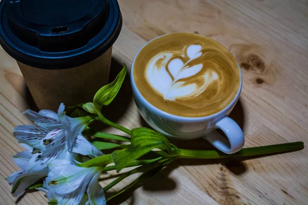 Cappuccino cup with latte art on table. The paper glass coffee and branch of white flowers. Caffeine. Morning. — Stock Photo, Image