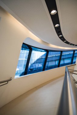 Modern binanın içinde. Eğimli ve yarım daire biçimli duvarlar, büyük pencereler ve balkon, aydınlatma ile. Mimarisi. Geometri.