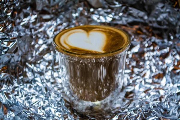 Cappuccino con arte latte en vidrio transparente con paredes dobles en el fondo de una lámina. Corazón. Bebida fuerte con cafeína . — Foto de Stock