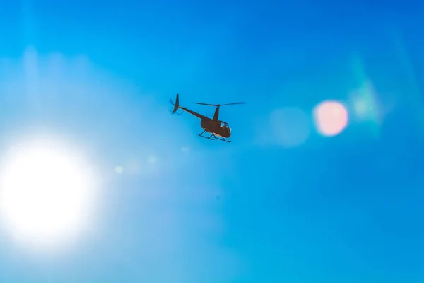 Silhueta de helicóptero no céu azul claro com manchas solares de luz. Dia quente da primavera. Transporte moderno . — Fotografia de Stock
