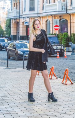 Bahar güneşli gün siyah giysili genç kızı eski şehir sokaklarında yürüyor. Elbise, ceket ve Mont. Modern moda.