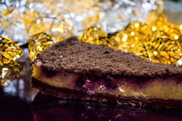 Piece of fresh home-made chocolate pie. Nearby yellow small lamps shine. Tasty pastries. — Stock Photo, Image