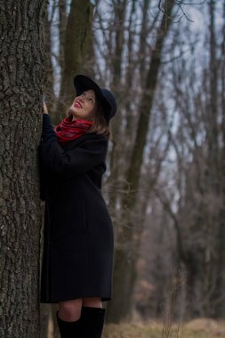 Siyah ceketli, kürek şapkalı ve dudaklarında kırmızı ruj olan kız parkta yürüyor. Stil ve modern moda.