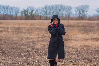 Siyah ceketli, kürek şapkalı ve dudaklarında kırmızı ruj olan kız parkta yürüyor. Stil ve modern moda.