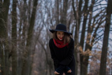 Siyah ceketli, kürek şapkalı ve dudaklarında kırmızı ruj olan kız parkta yürüyor. Stil ve modern moda.