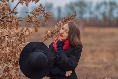 Siyah ceketli, kürek şapkalı ve dudaklarında kırmızı ruj olan kız parkta yürüyor. Stil ve modern moda.