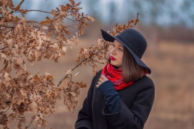 Siyah ceketli, kürek şapkalı ve dudaklarında kırmızı ruj olan kız parkta yürüyor. Stil ve modern moda.