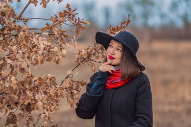 Siyah ceketli, kürek şapkalı ve dudaklarında kırmızı ruj olan kız parkta yürüyor. Stil ve modern moda.