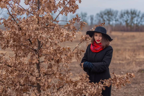 Siyah ceketli, kürek şapkalı ve dudaklarında kırmızı ruj olan kız parkta yürüyor. Stil ve modern moda.