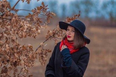 Siyah ceketli, kürek şapkalı ve dudaklarında kırmızı ruj olan kız parkta yürüyor. Stil ve modern moda.