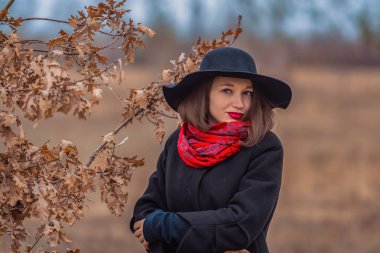 Siyah ceketli, kürek şapkalı ve dudaklarında kırmızı ruj olan kız parkta yürüyor. Stil ve modern moda.