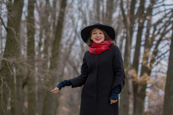 A menina com um casaco preto, um chapéu de pá e com batom vermelho nos lábios, caminha no parque. Estilo e moda moderna . — Fotografia de Stock