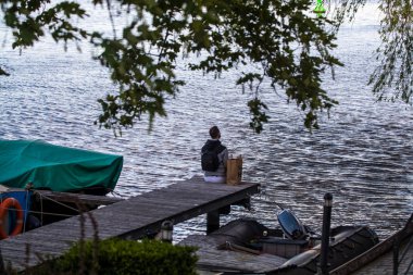 Sakallı genç ve şık adam nehir ve tekneler yakınında yürüyor. Düşünceli bir ruh hali. Suya bakar.