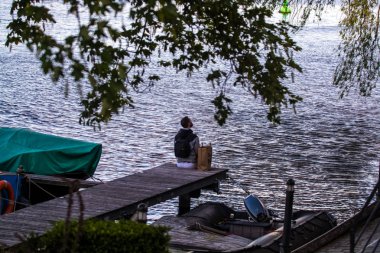Sakallı genç ve şık adam nehir ve tekneler yakınında yürüyor. Düşünceli bir ruh hali. Suya bakar.