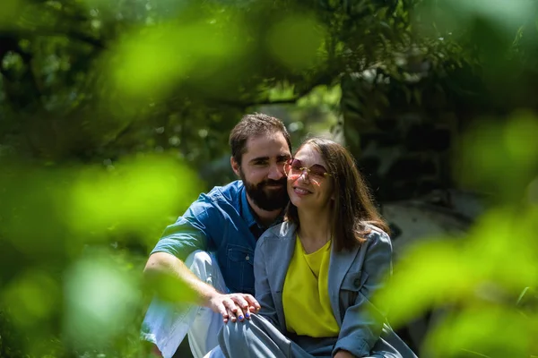 若くて現代的な愛情のあるカップルは 公園の緑の間に座っています 肯定的な感情 — ストック写真