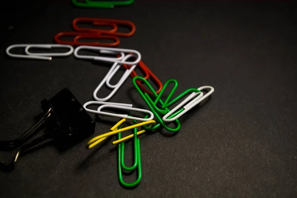 A set of multi-colored office paper clips of plastic are scattered on black monophonic background.