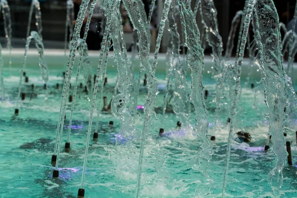 Big and strong water jets from the fountain with blue illumination in shopping center. Splashes and drops.