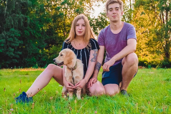 La joven pareja de enamorados casados pasea con el perrito en el parque. Golden retriever . —  Fotos de Stock