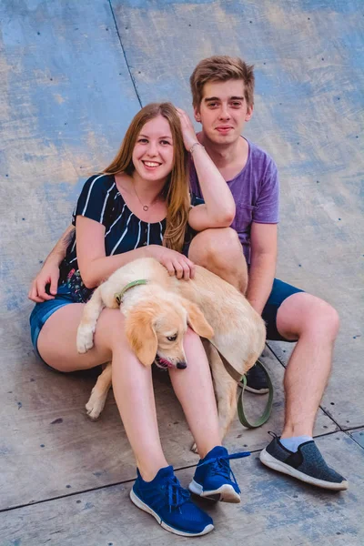 La joven pareja de enamorados casados pasea con el perrito en el parque. Golden retriever . —  Fotos de Stock