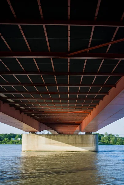 Die große und breite orangefarbene Automobilbrücke durch den Fluss in der Stadt. von unten. — Stockfoto