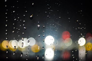 Arka plan veya doku. Pencerenin arkasında gece şehrinin öne çıkan ları ve yanları yağmur yağıyor.
