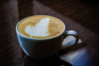 Parlak bir masada latte sanatı ile kapuçino beyaz bir fincan. Rozet.