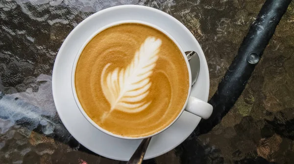 On glass table is white cup of cappuccino and latte art. Rosetta. Coffee shop and autumn. Morning coffee.