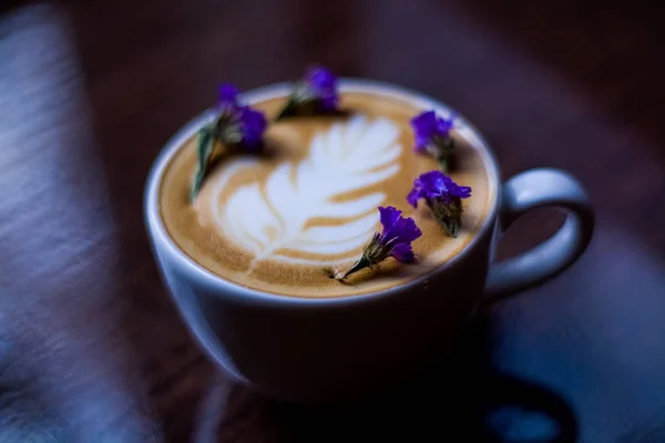 白色陶瓷杯卡布奇诺与拿铁艺术和小干和紫色花 咖啡店的早晨咖啡 — 图库照片