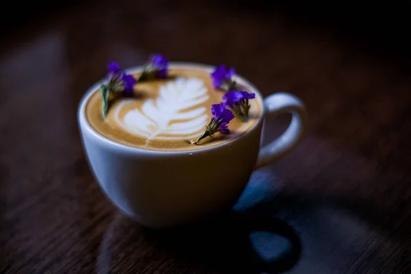 白色陶瓷杯卡布奇诺与拿铁艺术和小干和紫色花 咖啡店的早晨咖啡 — 图库照片