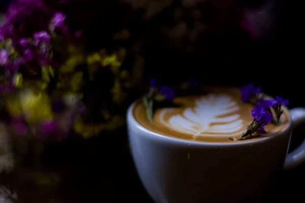 ラテアートと少し乾燥した紫色の花とカプチーノの白いセラミックカップ 喫茶店のモーニングコーヒー — ストック写真