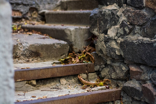 Background or texture of broken old, concrete steps on street with metal crossbars and fallen autumn, yellow leaves. Stone wall.