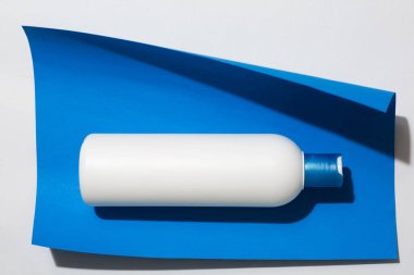 Beyaz plastik şişe, sıvı kozmetik için konteynır, mavi arka planda şampuan. Yazıtlar ve marka logosu için yer.