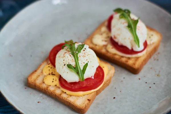 Tasty home breakfast of square toast with sliced fresh tomato and egg benedict with urugula.