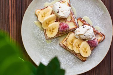 Büyük gri seramik tabak taze Belçika tatlı waffle 'ı, dondurma, çilek, muz ve konsantre süt. Lezzetli kahvaltı ve tatlı..