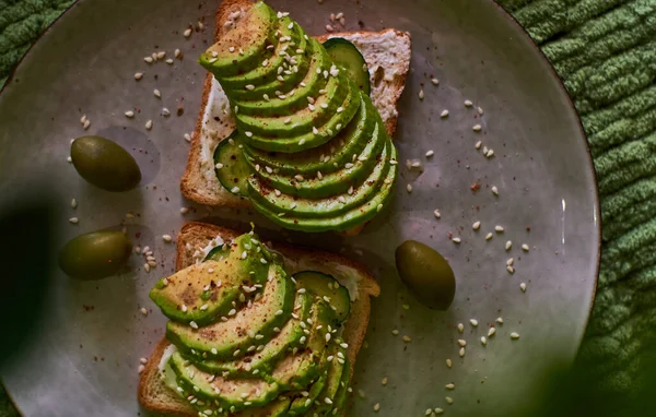 Tasty home breakfast of square toast with sliced fresh avocado, in green tones.