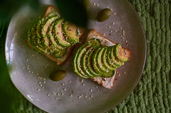 Tasty home breakfast of square toast with sliced fresh avocado, in green tones.