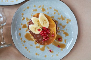 Kırmızı üzümlü taze ev yapımı krep ve gri tabakta karamel ve siyah ve koyu kahveyle el yapımı arka plan. Lezzetli kahvaltı ve hamur işleri.