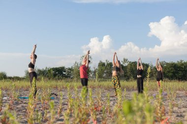 group yoga performing sun salutations outdoors