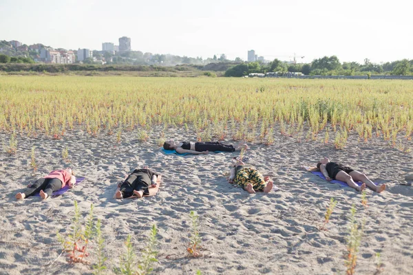 Group of students performing yoga nidra on sand — Stock Fotó