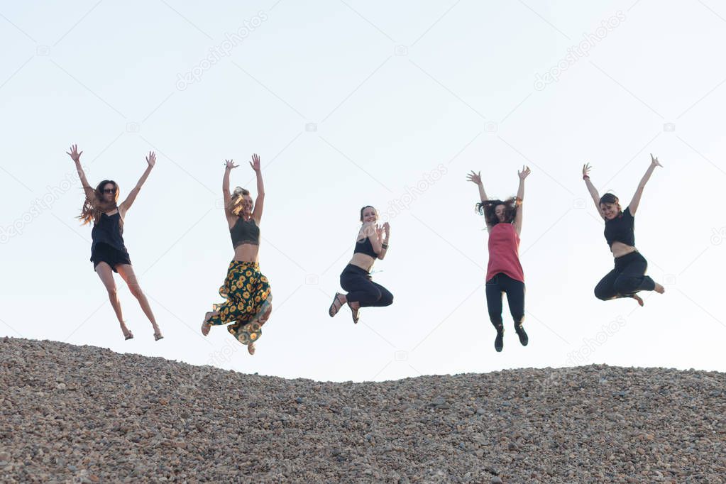 five girlfriends jumping together with joy on pebble hill