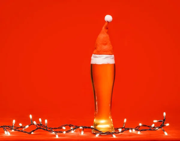 全皮包罐杯苍白的啤酒或啤酒与圣诞老人或圣诞节红色帽子和圣诞灯在红色背景 — 图库照片