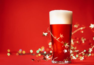 Bardak bardak soluk lager bira veya ale ile koca kafa köpük ve Noel ışıkları ve tinsel kırmızı zemin üzerine