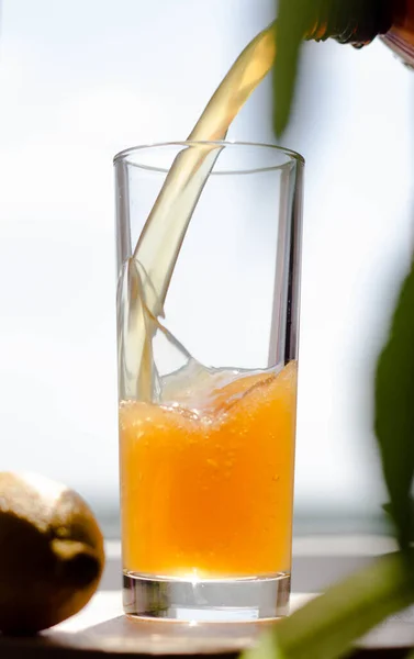 A yellow foaming drink is poured into a glass from a dark bottle. The brew in the glass
