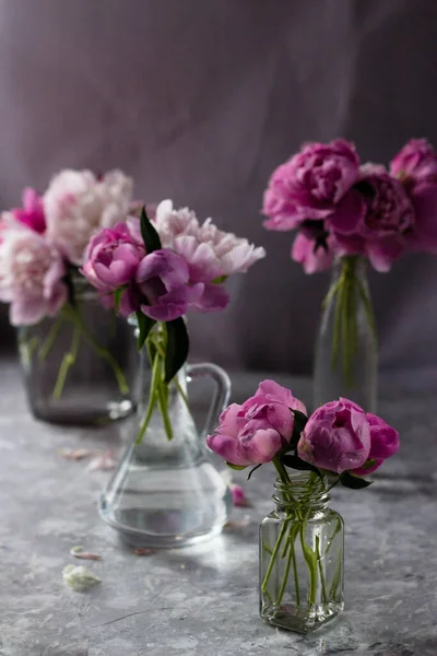 Pink flowers in glass containers on a light background. Lush peonies and buds in glass bottles