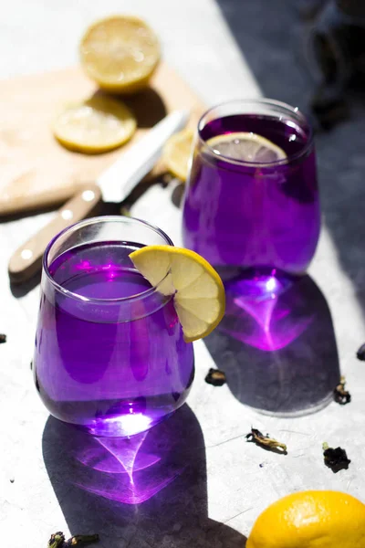 the glasses are filled with a purple drink with lemon on top in the rays of the bright sun. Purple tea in glasses, next to pieces of lemon