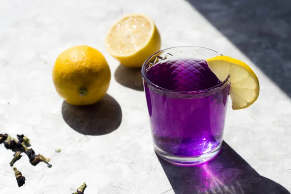 the glasses are filled with a purple drink with lemon on top in the rays of the bright sun. Purple tea in glasses, next to pieces of lemon