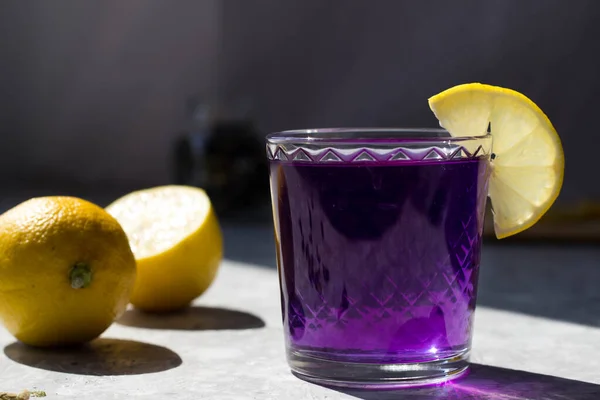 the glasses are filled with a purple drink with lemon on top in the rays of the bright sun. Purple tea in glasses, next to pieces of lemon