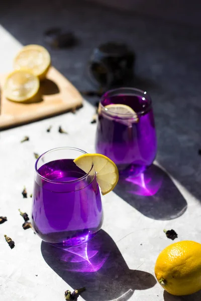 the glasses are filled with a purple drink with lemon on top in the rays of the bright sun. Purple tea in glasses, next to pieces of lemon