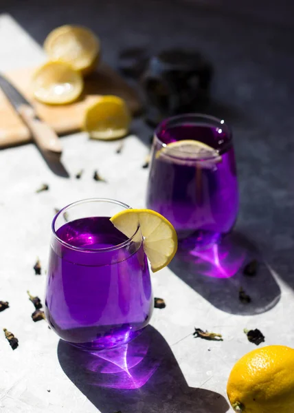 the glasses are filled with a purple drink with lemon on top in the rays of the bright sun. Purple tea in glasses, next to pieces of lemon